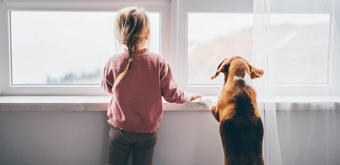 Dog and baby girl staring out a large window. best dog breeds for kids